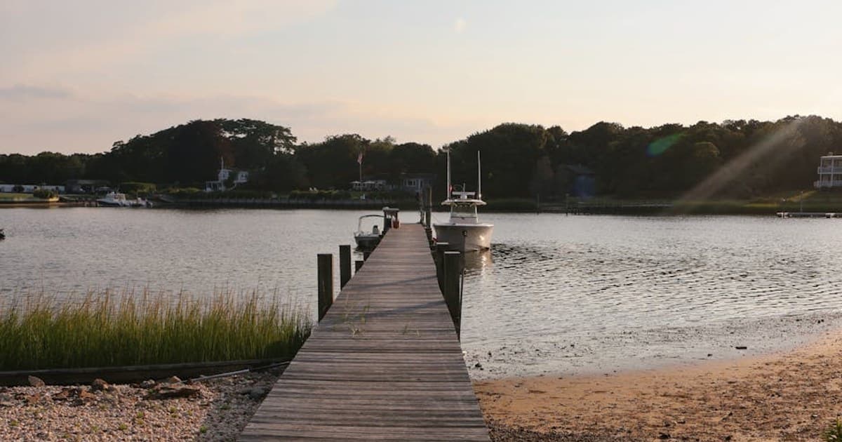Serene wooden pier at sunset in Hampton Bays, NY, leading to calm waters.