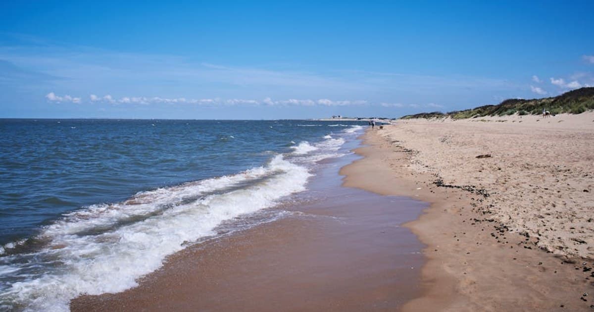 Sunny beach at Knokke-Heist, Belgium, with small waves and clear blue sky.