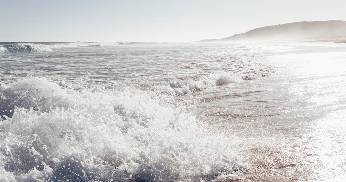 Tranquil scene of ocean waves crashing against a sandy seashore under a clear sky.