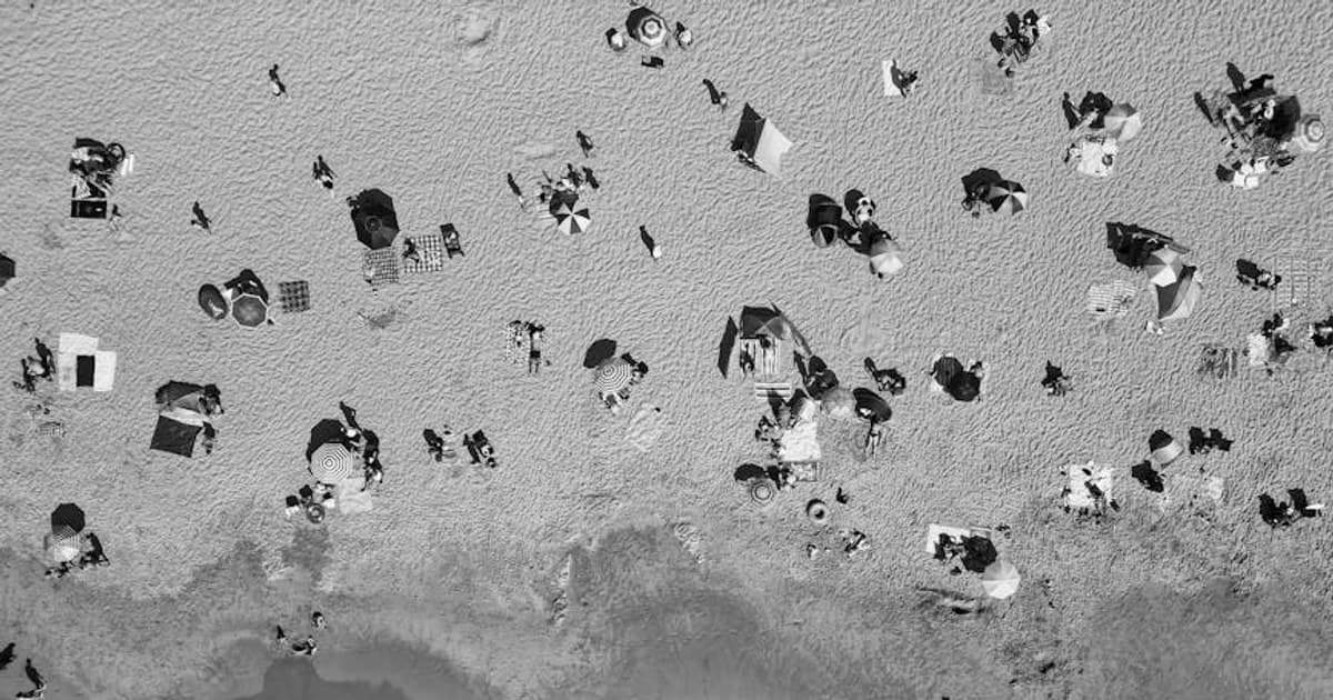 Black and white aerial view of a beach with umbrellas and people creating a lively scene.