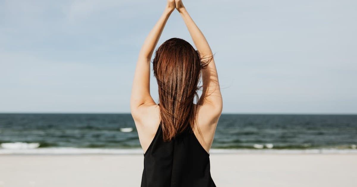 Back view of a woman practicing yoga by the sea, embracing peace and tranquility.