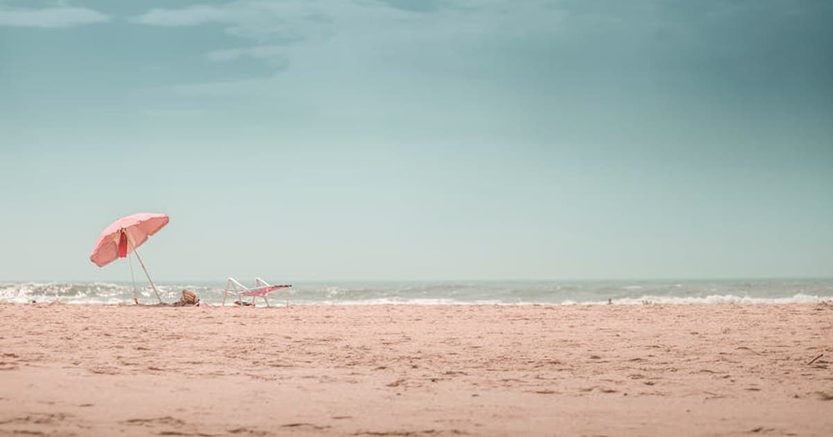 Peaceful beach with pink umbrella and sand, perfect for a summer escape.
