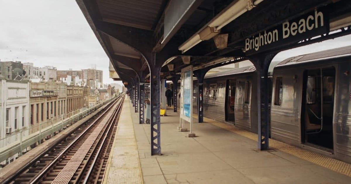 View of Brighton Beach train station platform with train and cityscape in the background.