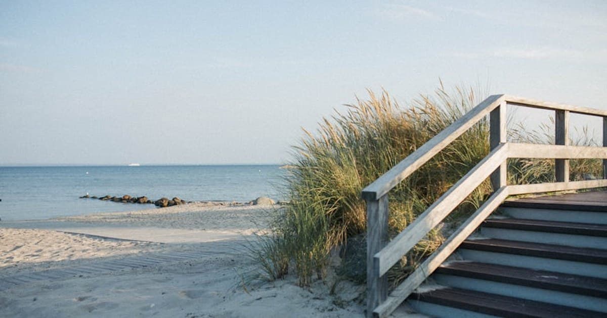 Scenic view of a wooden pathway leading to a tranquil sandy beach with gentle ocean waves.