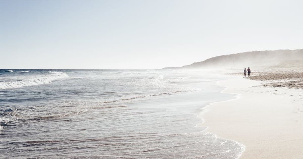 A couple walking along a peaceful beach with gentle waves during sunset.