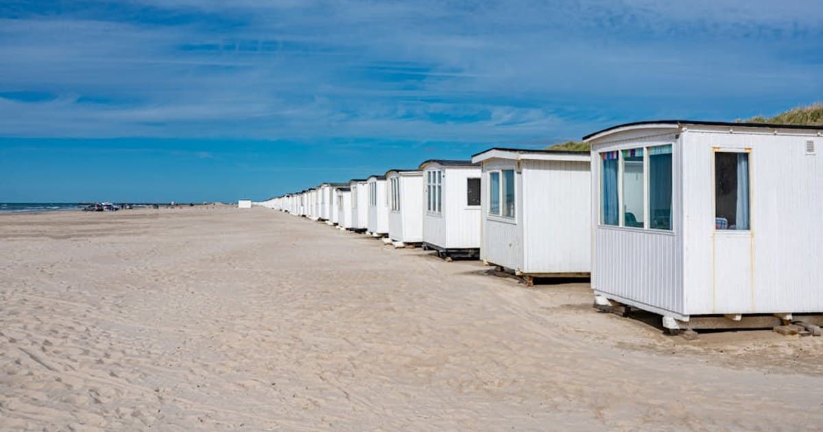 A row of white beach cabins along the sandy coast of Løkken, Denmark.