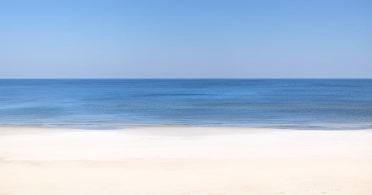A tranquil beach scene with clear blue skies and calm ocean waves.