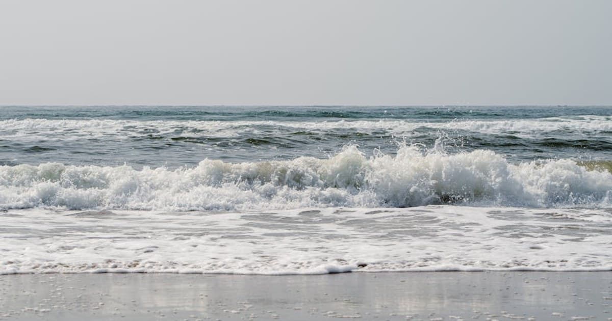 Capture of waves crashing on a quiet beach shoreline under a clear sky.