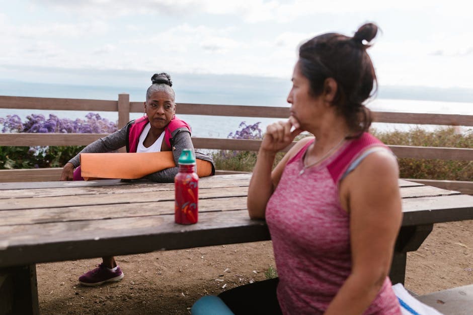 Two women resting by the beach after yoga, enjoying a serene outdoor setting.