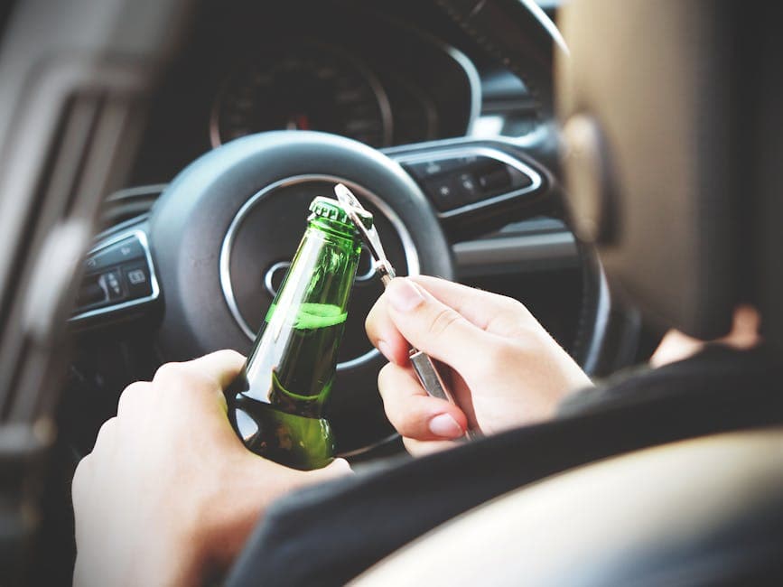 Hands opening a beer bottle inside a car, highlighting the importance of safe driving and awareness of road dangers.