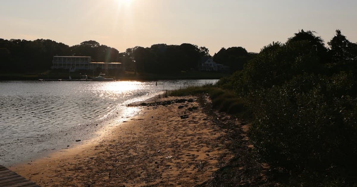 Golden sunset over Hampton Bays beach with serene water reflection.