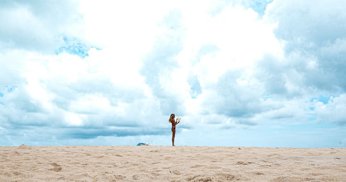 A woman practicing yoga on a sandy beach in Natal, Brazil. Bright skies create a serene backdrop.