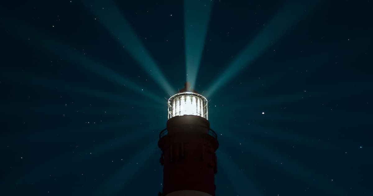 A lighthouse beams light across a starry night sky, creating an ethereal glow over the sea.